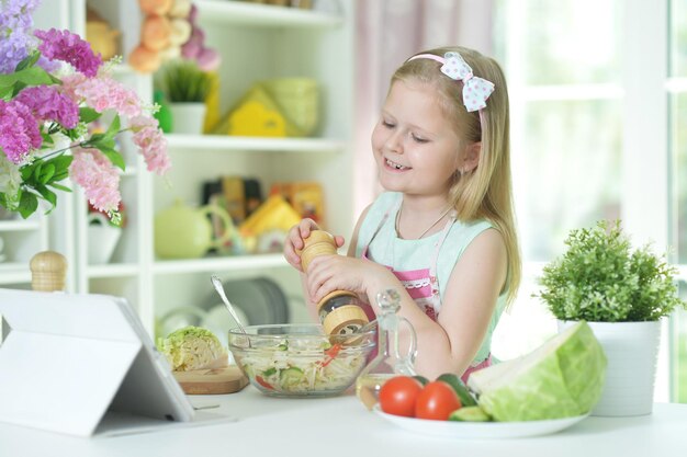 Schattig klein meisje pittige salade op keukentafel