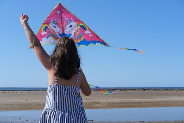 Schattig klein meisje regenboog vlieger vliegen op zee strand.