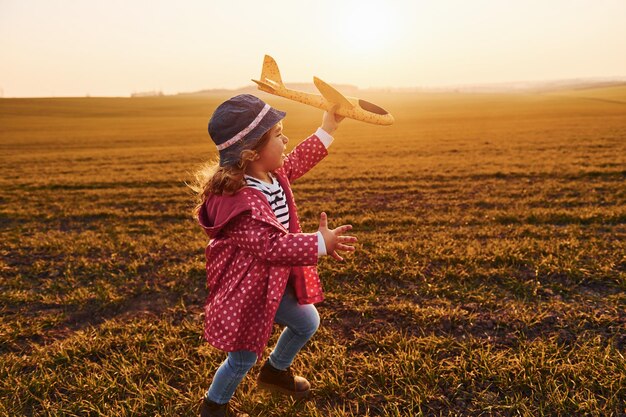 Schattig klein meisje rent met speelgoedvliegtuig op het prachtige veld op zonnige dag