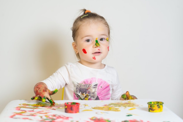 Schattig klein meisje speelt met gekleurde verf op een witte achtergrond