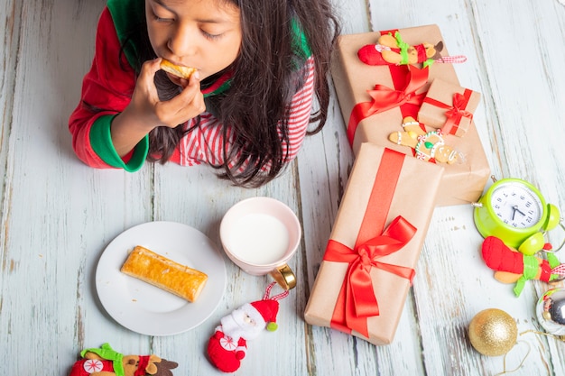 Schattig klein meisje speelt met kerstkoekjes en melk met Kerstmis