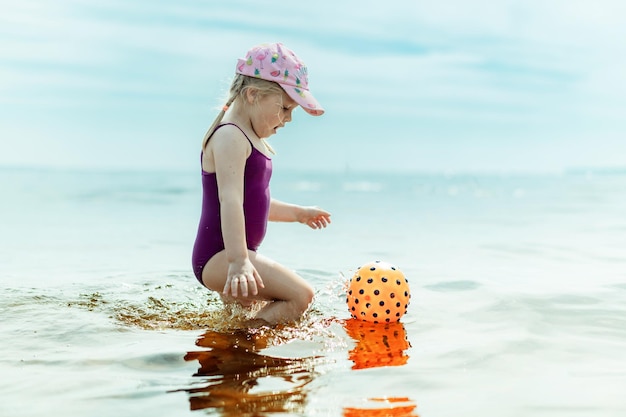 Schattig klein meisje speelt met rubberen bal in zee