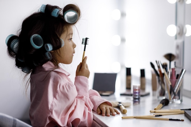 Schattig klein meisje speelt thuis met de cosmetica van haar moeder voor de spiegel