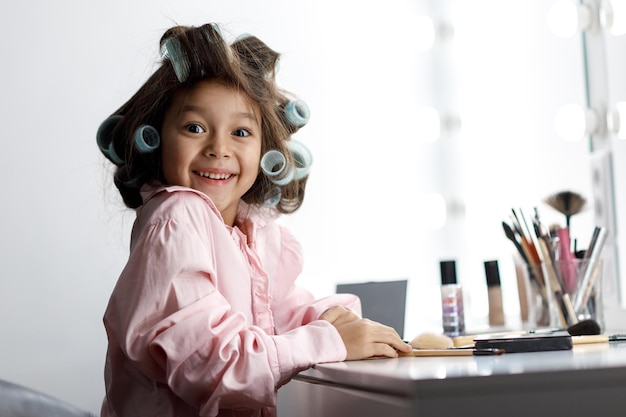 Schattig klein meisje speelt thuis met de cosmetica van haar moeder voor de spiegel