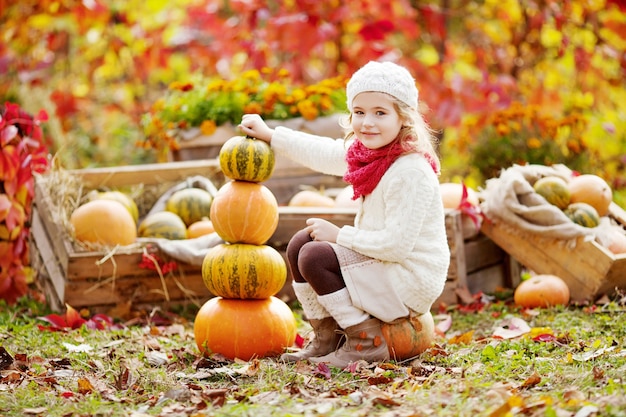 Schattig klein meisje spelen met pompoenen in herfst park. Herfstactiviteiten voor kinderen. Schattig klein meisje bouwt een toren van pompoenen. Halloween en Thanksgiving tijd plezier voor familie.