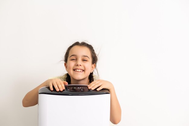 Schattig klein meisje staande ademhaling bij luchtreiniger. Schone luchtconcept.