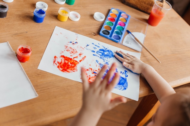 Schattig klein meisje tekent met verf en handen Geschilderde handpalmen voor kinderen