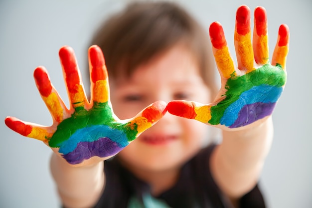 Schattig klein meisje toont haar handen met regenboog geschilderd op haar handpalmen