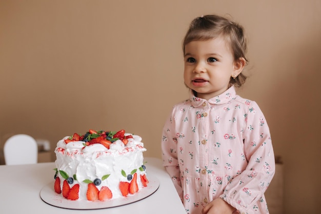 Schattig klein meisje van een en een half jaar oud staat bij heerlijke verjaardagstaart Achttien maanden oud meisje heel blij en lacht Vegetarisch eten Lactosevrij en glutenvrij