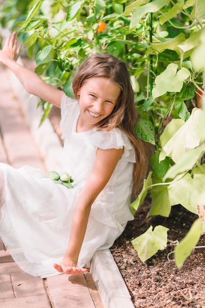 Schattig klein meisje verzamelt gewas komkommers en tomaten in kas