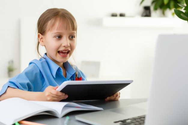 Schattig klein meisje zit aan tafel met haar laptop en studeert online