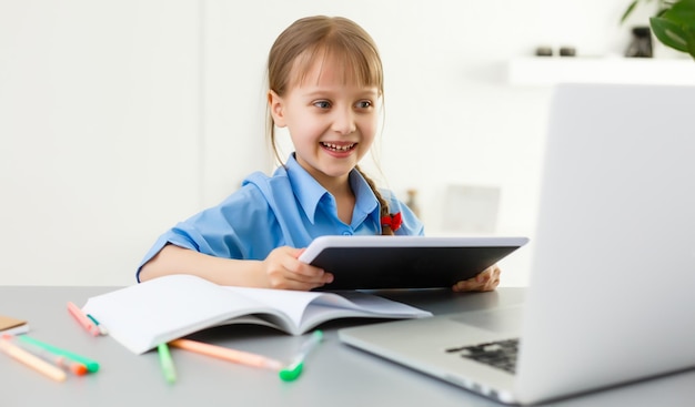 Schattig klein meisje zit aan tafel met haar laptop en studeert online