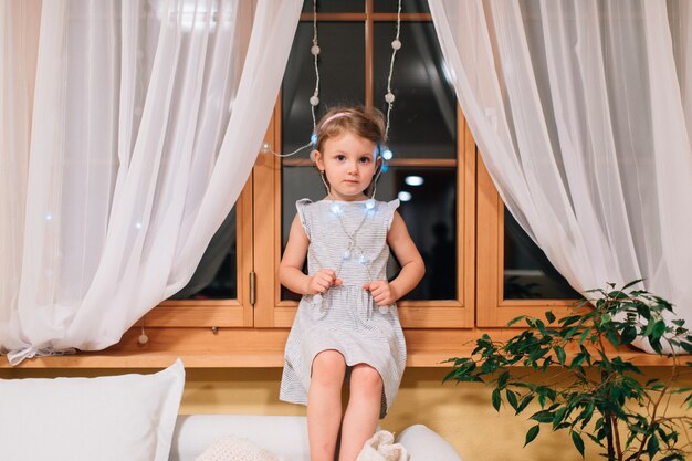 Schattig klein meisje zit in haar kamer op een vensterbank 's nachts.