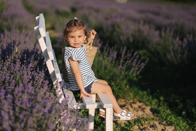 Schattig klein meisje zit op bankje in lavendelveld Zomerzonsondergang