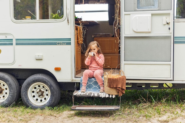 Schattig klein meisje zit op de trappen van een camper en drinkt warme chocolademelk met marshmallows