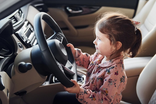 Schattig klein meisje zittend op de bestuurdersstoel binnenkant van moderne auto