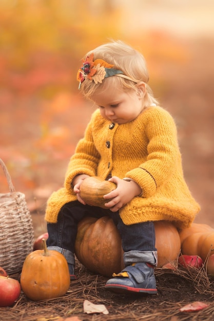 Schattig klein meisje zittend op pompoen en spelen in herfst bos