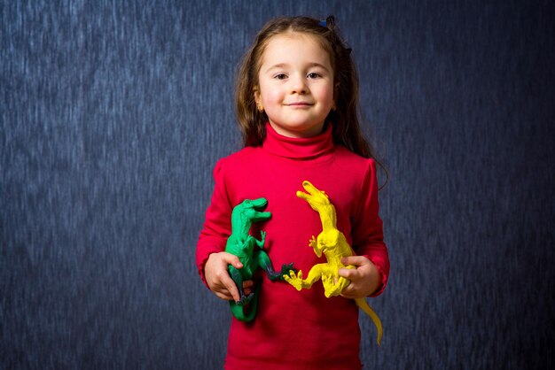 Schattig klein meisjesspel met speelgoeddinosaurussen op de blauwe achtergrond