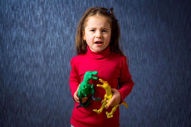 Schattig klein meisjesspel met speelgoeddinosaurussen op de blauwe achtergrond