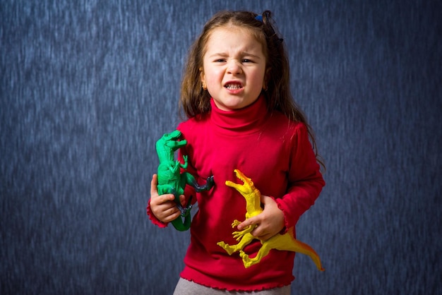Schattig klein meisjesspel met speelgoeddinosaurussen op de blauwe achtergrond