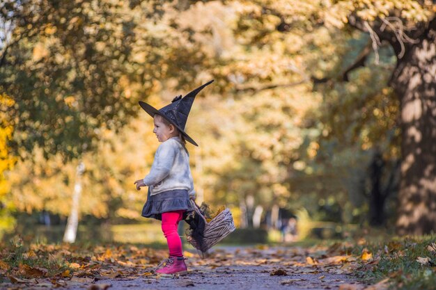 Schattig klein peutermeisje in het herfstparkmeisje in heksenkostuum en zwarte hoed cosplay halloween