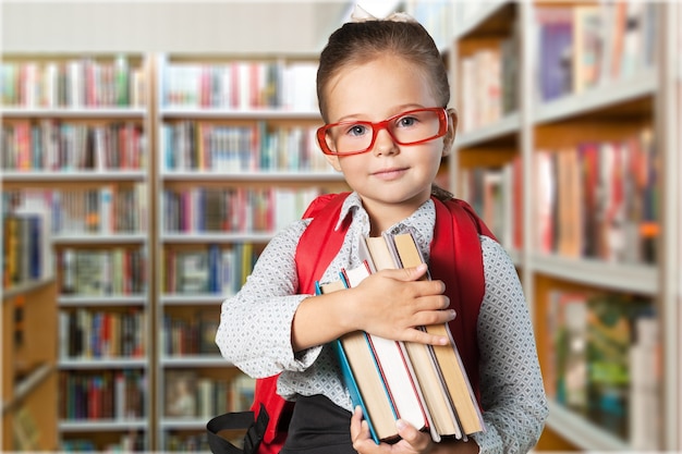 Schattig klein schoolmeisje in glazen op bibliotheekachtergrond