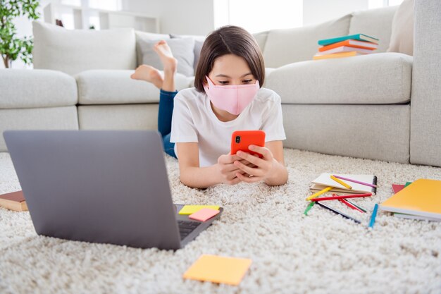 schattig klein schoolmeisje met medisch masker houdt telefoon vast