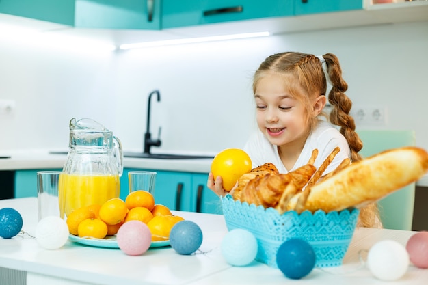 Schattig klein speels grappig meisje dat graag oranje sinaasappels vasthoudt, met keuken op de achtergrond