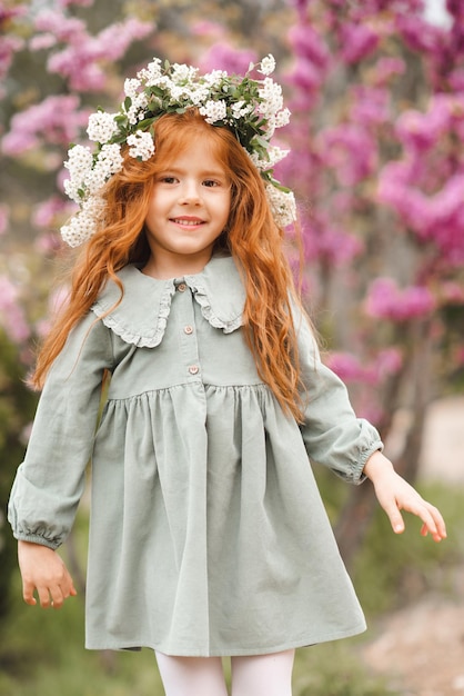 Schattig lachend klein kind meisje 3-4 jaar oud draag bloemenkrans en stijlvolle rustieke jurk over de natuur