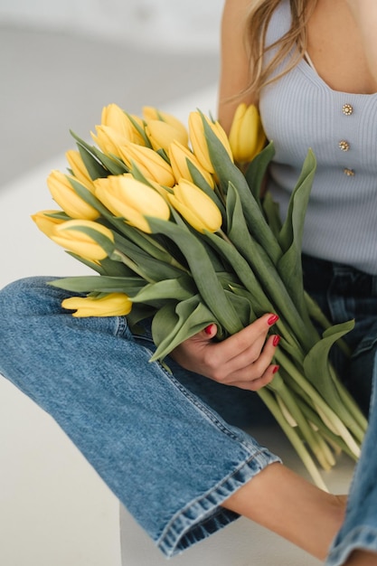 Schattig lachend meisje met een boeket gele tulpen in het interieur