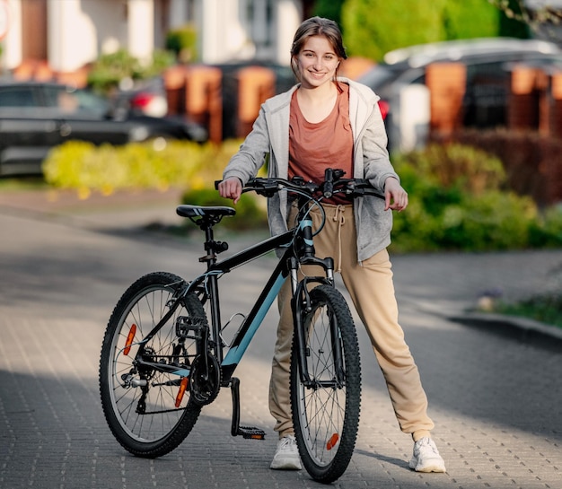 Schattig lachend meisje met een fiets 's avonds in een rustige stad tegen het huis
