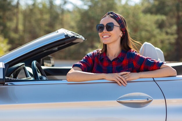 Schattig lachend meisje met een zonnebril in de auto zitten en wegkijken