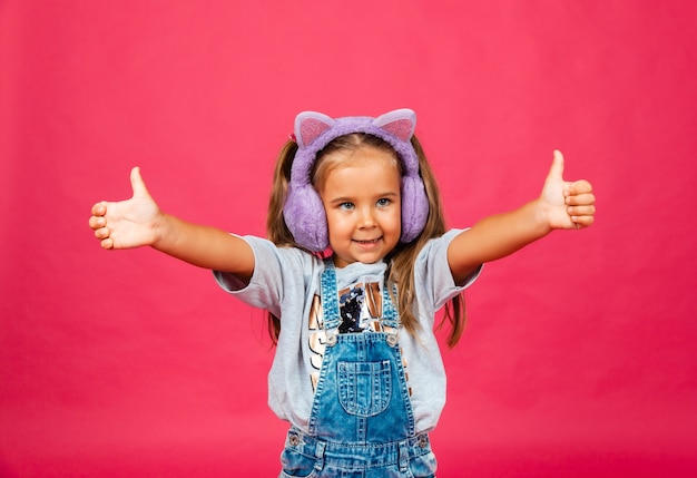 Schattig lachend meisje met plezier in bont koptelefoon op een roze achtergrond.