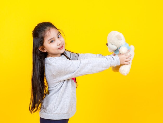 Schattig liitlw Aziatisch meisje houden en spelen met teddy blote pop op gele achtergrond. Concept van grappig kind en verbeelding.