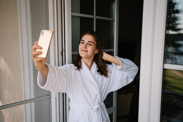 Schattig meisje in badjas neemt selfie op balkon