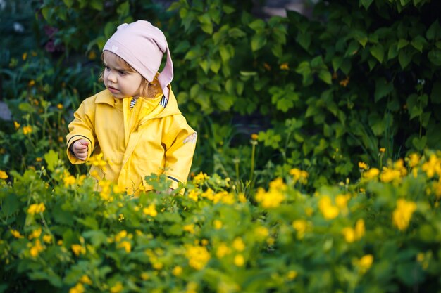 Schattig meisje in een geel jasje verzamelt bloemen in een weide. Een kind stond in het frisse groene gras tussen de lentebloemen. Een klein kind maakt een boeket van de eerste wilde gele bloemen