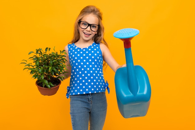 Schattig meisje in glazen heeft een blad plant in haar handen en een gieter op een gele muur