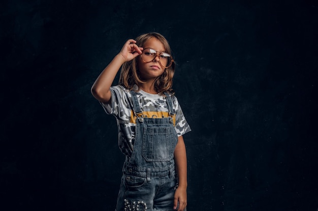 Schattig meisje in grote glazen poseert voor fotograaf in donkere fotostudio.