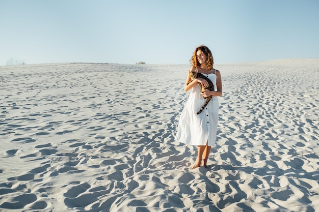 Schattig meisje in witte jurk op het strand knuffelt haar Bengaalse kat