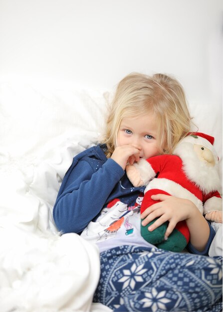 Schattig meisje is opgewonden liggend op een witte achtergrond en houdt de kleine kerstman vast, kerstvakantie