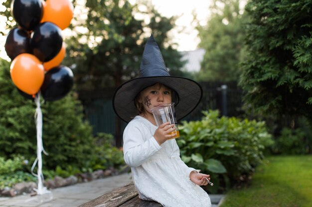 Foto schattig meisje met heksenhoed drinkt sap op halloween-feest