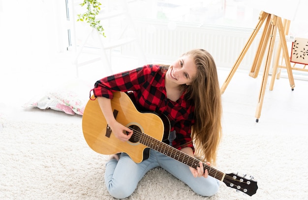 Schattig meisje met lang los haar gitaar spelen in lichte kamer