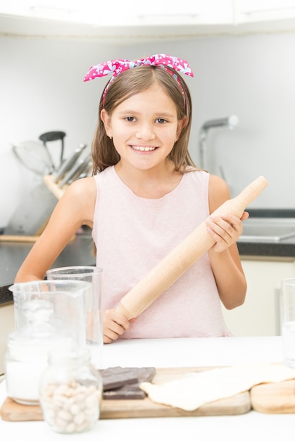 Schattig meisje met roze strik op haar poseren met houten deegroller