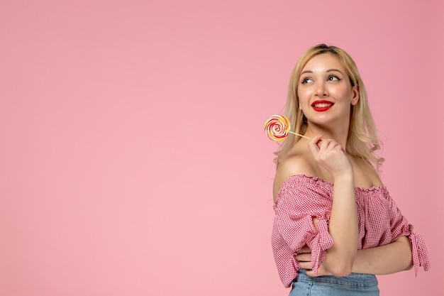 Schattig meisje, mooie jonge dame met rode lippenstift in roze blouse met het zoete snoepje dat omhoog kijkt