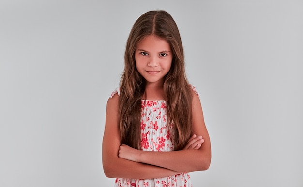 Foto schattig meisje op een grijze achtergrond in jurk vouwde haar armen en beledigd, boos, ondeugend