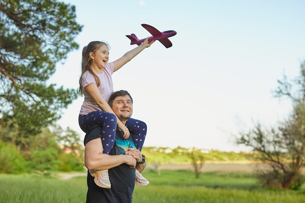 Schattig meisje rijdt op vaders schouder en speelt met speelgoedvliegtuig