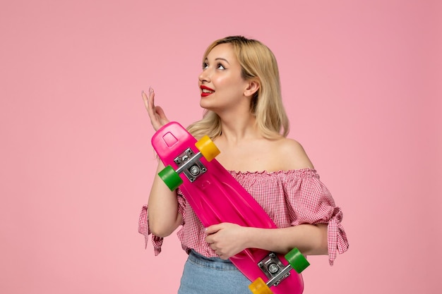 Schattig meisje schattig kuiken met rode lippenstift in roze blouse in de lucht kijken met skateboard