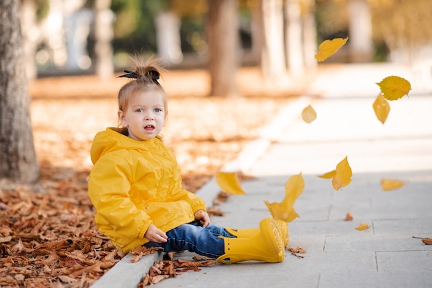 Schattig meisje van 2-3 jaar oud draagt een gele regenjas en rubberen laarzen in het herfstpark buiten