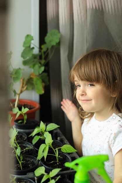 Schattig meisje van 2 jaar oud is thuis in de buurt van zaailingen van groenten en kruiden