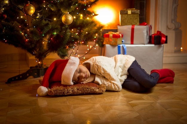 Schattig meisje viel in slaap onder de kerstboom tijdens het wachten op de kerstman